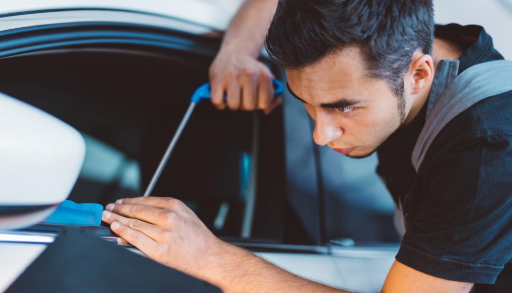 Young male mechanic focused on detailing a black car tire in an automotive garage.