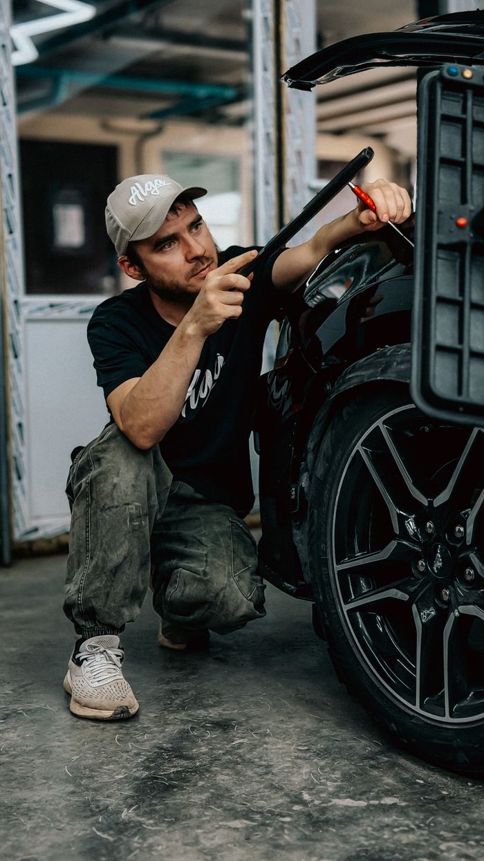Young male mechanic focused on detailing a black car tire in an automotive garage.